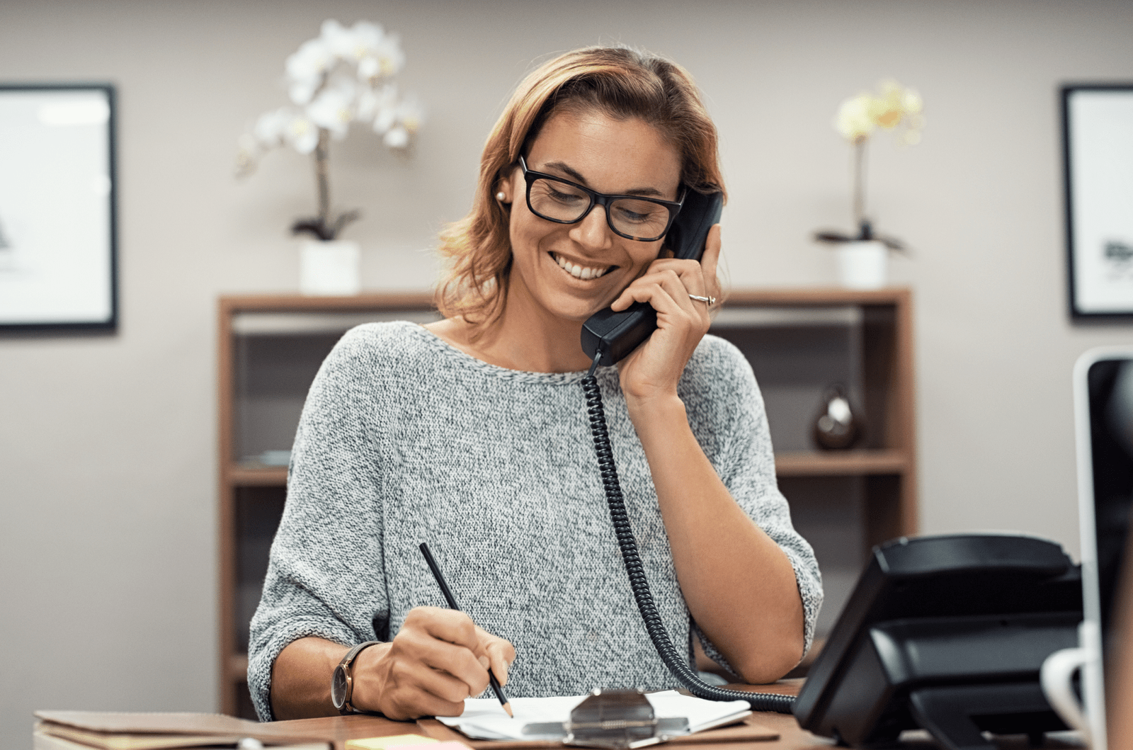 Professional answering service worker on phone taking notes.